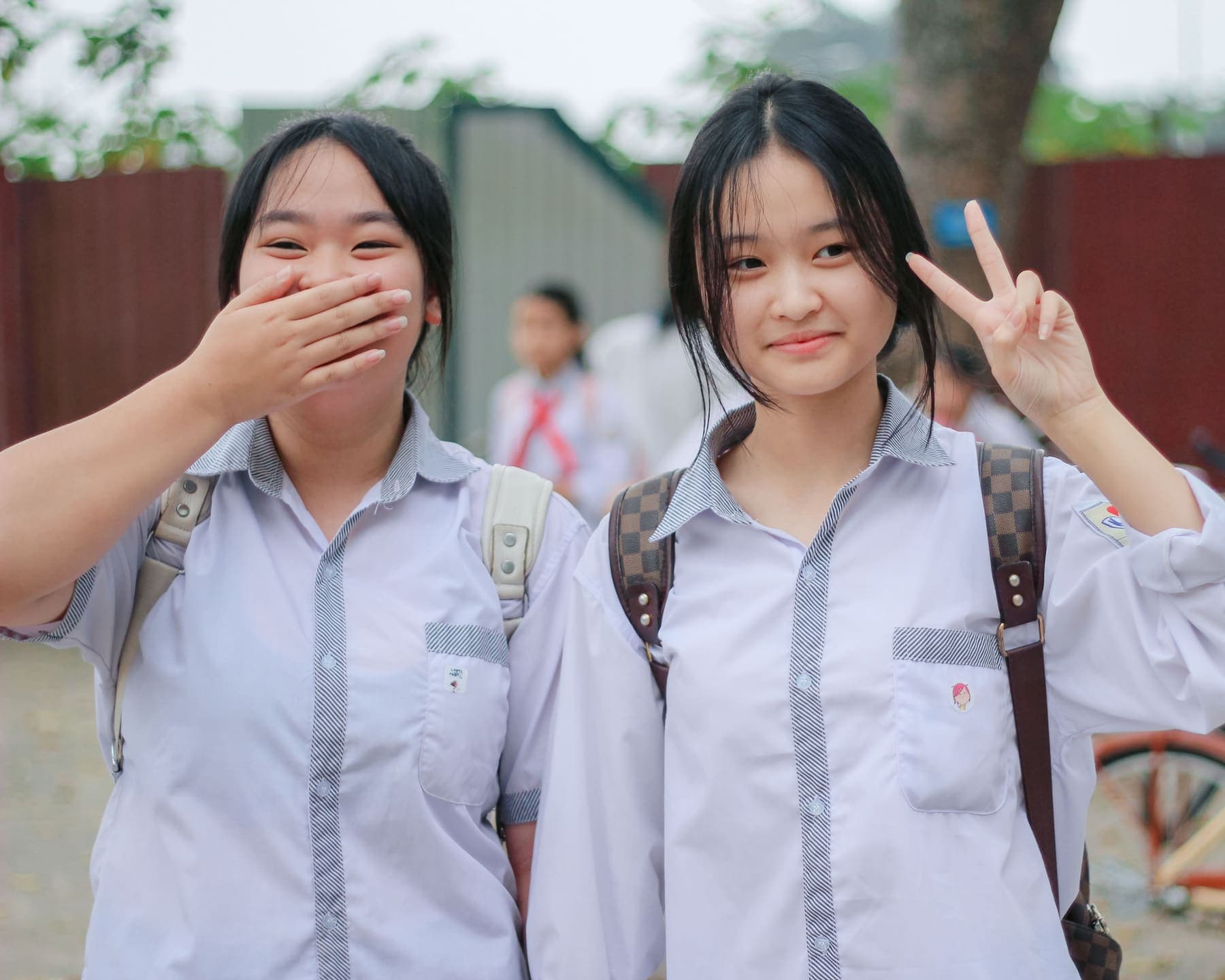 Two students in school uniform smiling together outside the school gates at the end of the day